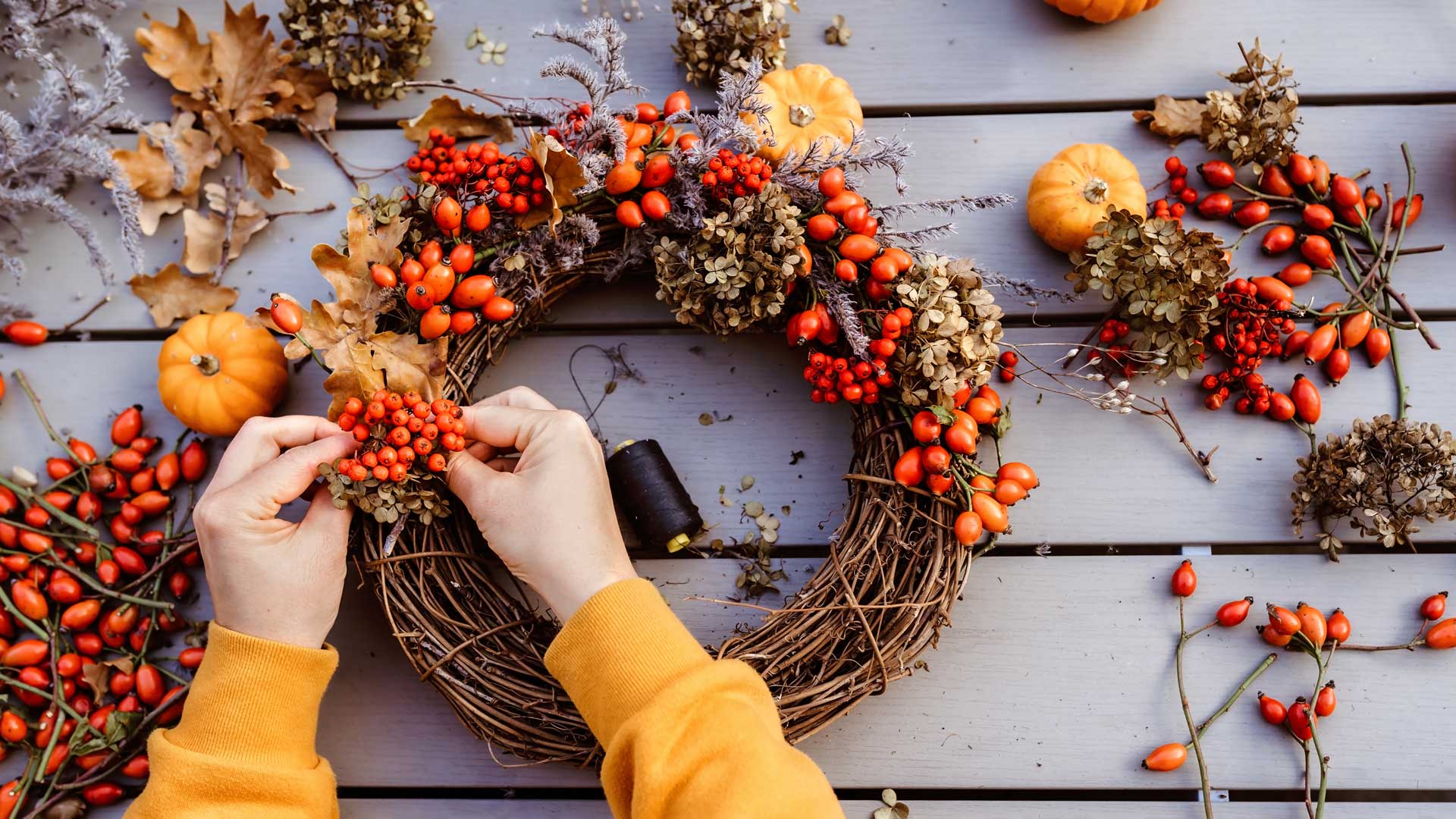 Girl making floral autumn door wreath using colorful rosehip berries.