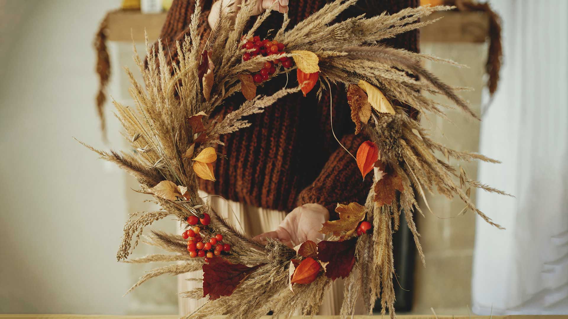 Woman holding autumn wreath in rustic room.