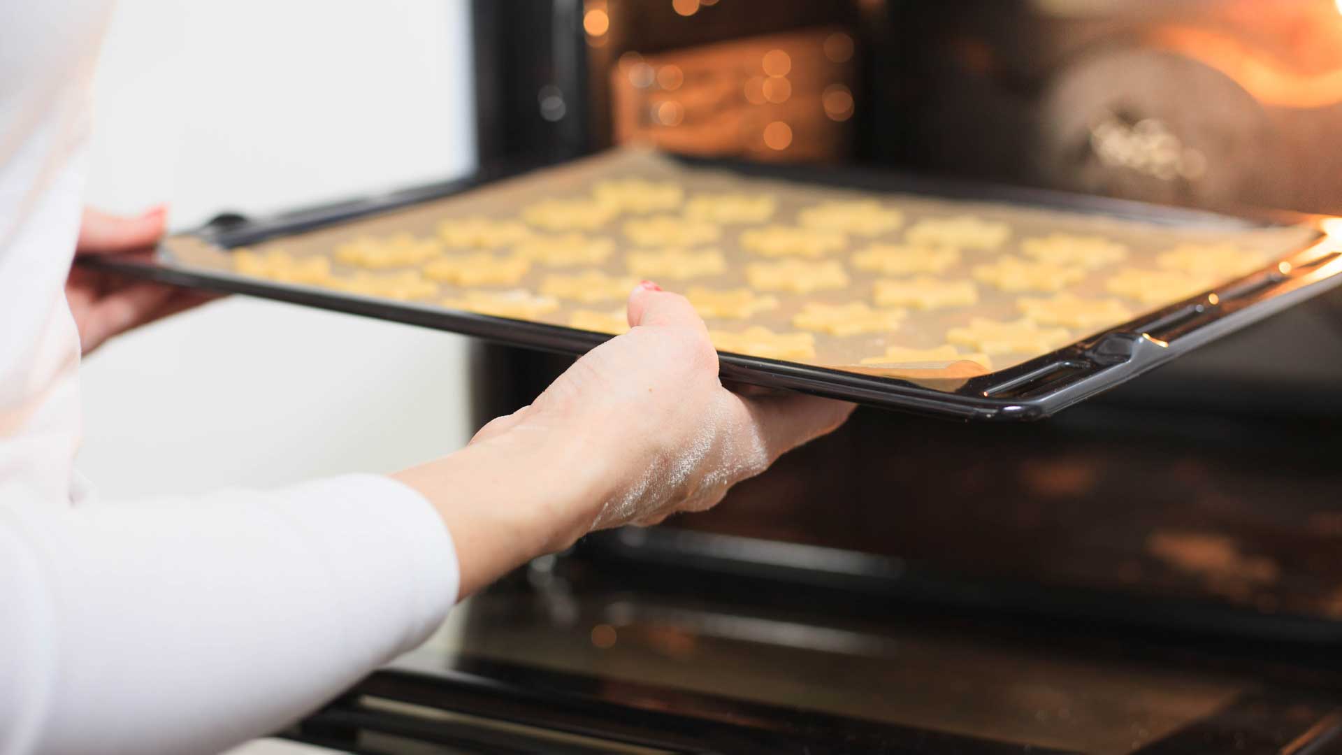 Young hands giving baking sheet of ginger to hot oven.